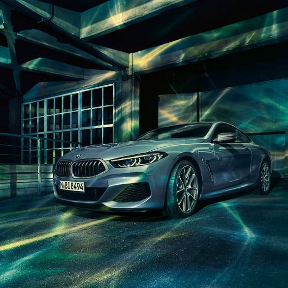BMW M850i xDrive Coupé, three-quarter front view. BMW M850i xDrive Coupé in Barcelona Blue metallic, three-quarter front view standing in front of building.