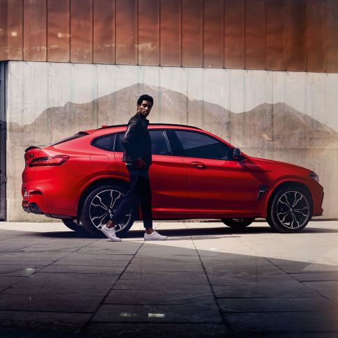 BMW X4 M, side view with young man. BMW X4 M in Toronto Red metallic, exterior, side view with young man.