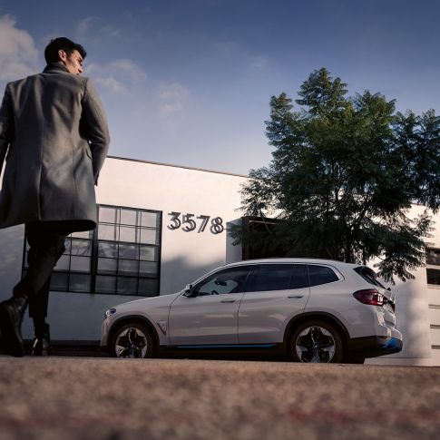 BMW iX3 G08 side view in front of building with man BMW iX3 G08 2020 Mineral White metallic side view in front of building with man
