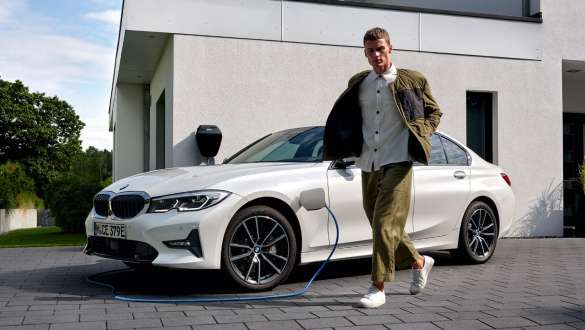 มุมมองด้านหน้าแบบ 3/4 ของ BMW ซีรีส์ 3 Sedan G20 ระบบปลั๊กอินไฮบริดรุ่นปี 2021 ขณะกำลังชาร์จ มุมมองด้านหน้าแบบ 3/4 ของ BMW ซีรีส์ 3 Sedan G20 ระบบปลั๊กอินไฮบริดรุ่นปี 2021 ขณะกำลังชาร์จพร้อมนายแบบ