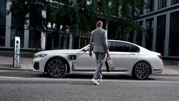 BMW 745e Sedan plug-in hybrid G11 G12 Mineral White metallic side view at charging point BMW 745e Sedan plug-in hybrid G11 G12 Mineral White metallic side view in front of charging point with model