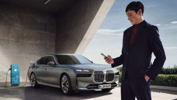 การ์ด BMW Charging ของ BMW i7 Sedan G70 การ์ด BMW Charging เบื้องหน้าพร้อม BMW i7 Sedan G70 สี Oxid grey metallic จาก BMW Individual ที่กำลังชาร์จในฉากหลัง