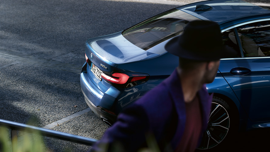 BMW ซีรีส์ 5 Sedan (G30) สี Phytonic Blue metallic BMW ซีรีส์ 5 Sedan (G30) สี Phytonic Blue metallic บนลานจอดรถ มีคนอยู่ด้านหน้า
