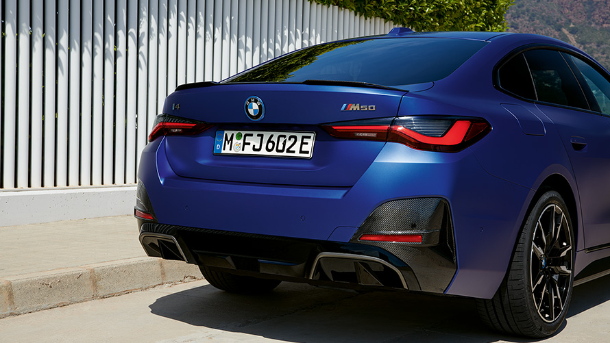 มุมมองด้านหลังแบบ 3/4 ของ BMW i4 M50 G26 2021 สี Frozen Portimao Blue metallic จาก BMW Individual จอดหน้ารั้วสีขาว