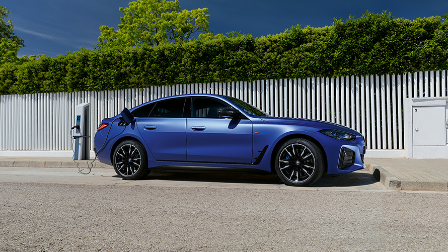มุมมองด้านข้างของ BMW i4 M50 G26 2021 สี Frozen Portimao Blue metallic จาก BMW Individual ขณะเชื่อมต่อกับเสาชาร์จ