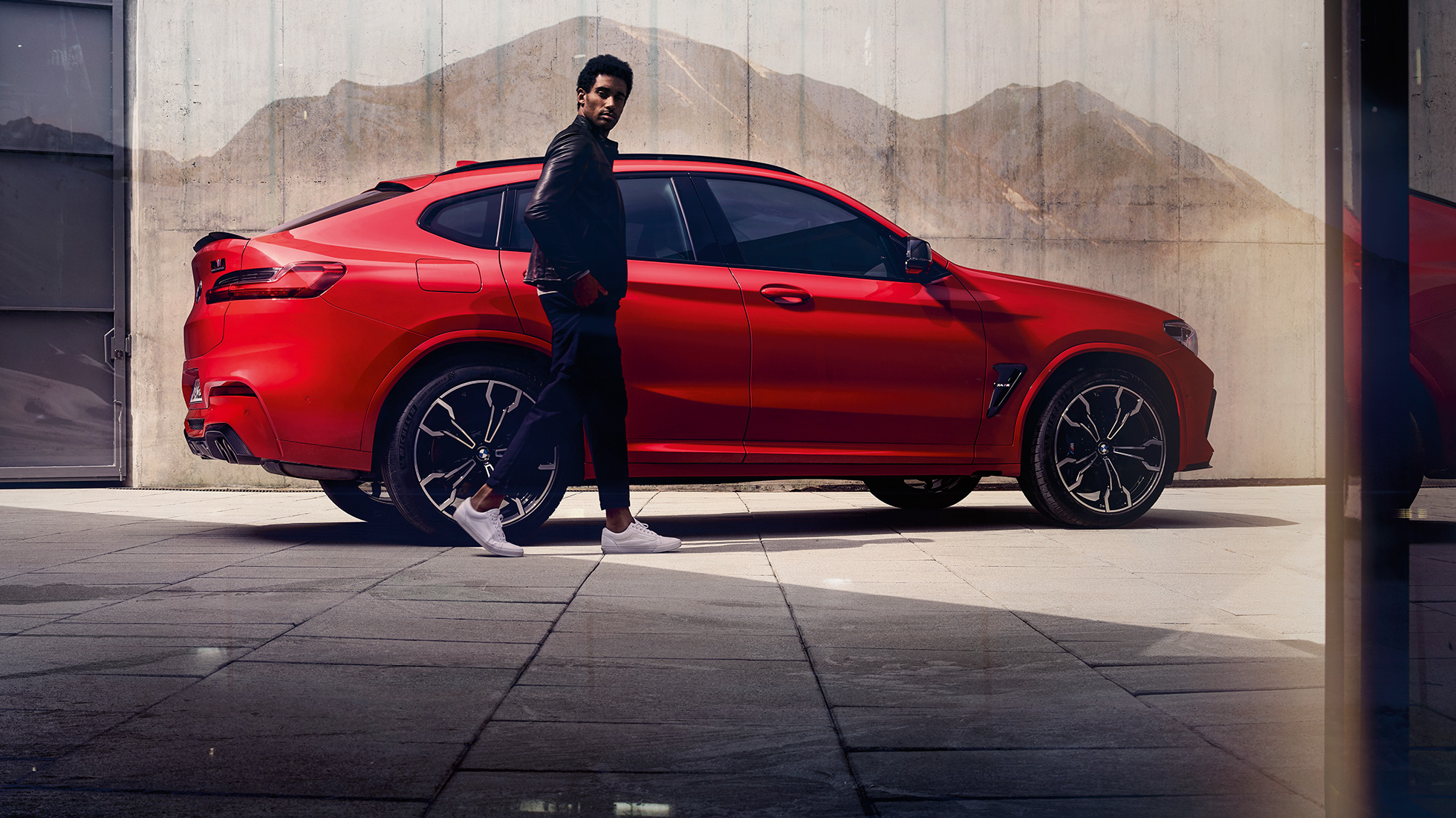 BMW X4 M, side view with young man. BMW X4 M in Toronto Red metallic, exterior, side view with young man.
