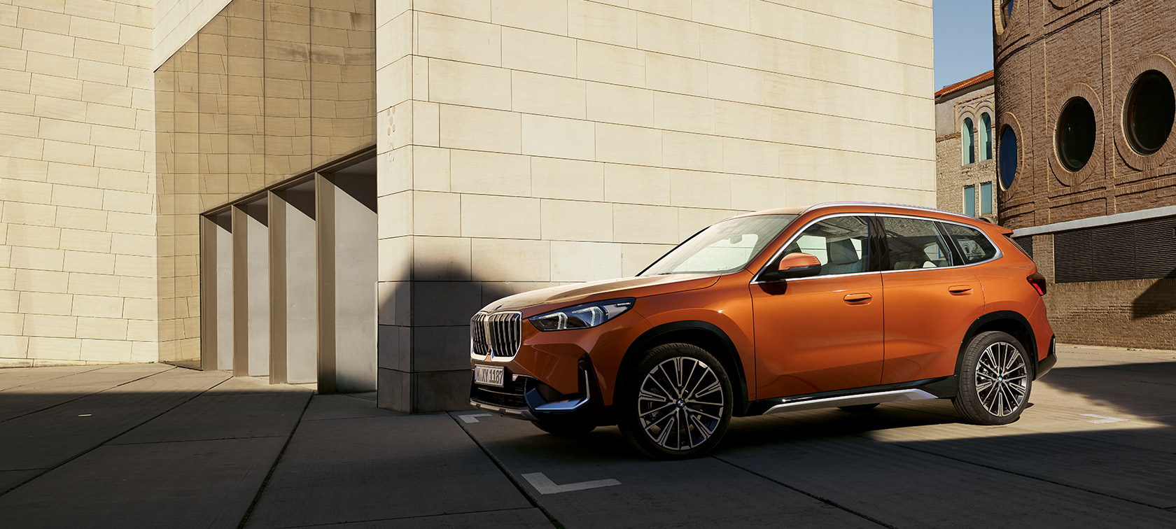 BMW U11 X1 xLine สี Utah orange metallic มุมมองด้านหน้าแบบ 3/4 BMW U11 X1 xLine สี Utah orange metallic มุมมองด้านหน้าแบบ 3/4 จอดอยู่หน้าอาคาร