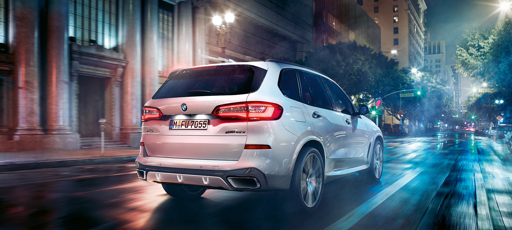 มุมมองด้านหลังแบบสามในสี่ส่วนของ BMW X5 ขณะขับขี่ มุมมองด้านหลังแบบสามในสี่ส่วนของ BMW X5 G05 2018 สี Mineral White metallic ขณะขับขี่