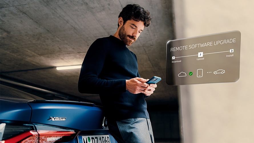 Remote Software Upgrade Man leans against rear of BMW and looks at his smartphone
