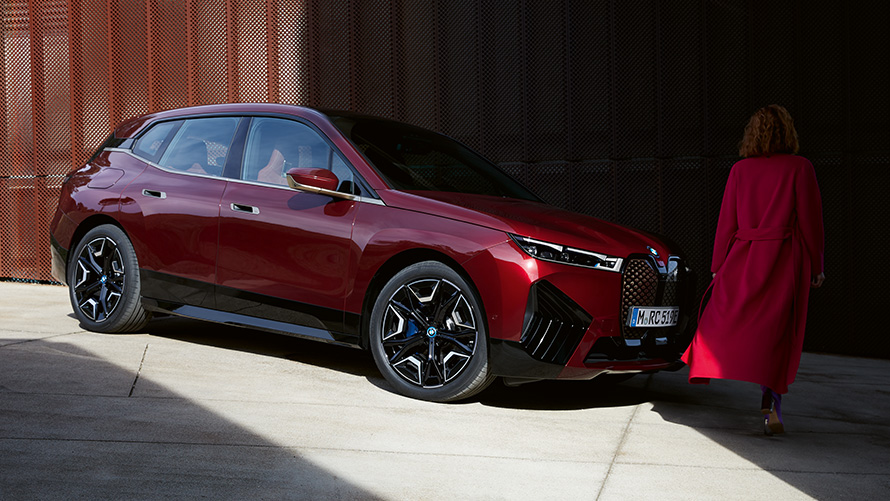 นางแบบอยู่ด้านหน้า BMW iX i20 2021 มุมมองด้านหน้าแบบ 3/4 นางแบบในเสื้อโค้ทสีแดงอยู่ด้านหน้า BMW iX i20 2021 มุมมองด้านหน้าแบบ 3/4