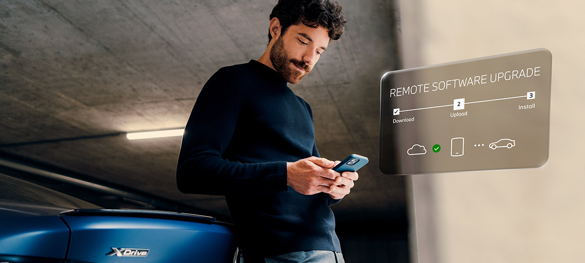 ผู้ชายยืนพิงท้ายรถยนต์ BMW ขณะดูสมาร์ทโฟน Remote Software Upgrade ผู้ชายยืนพิงท้ายรถยนต์ BMW ขณะดูสมาร์ทโฟน