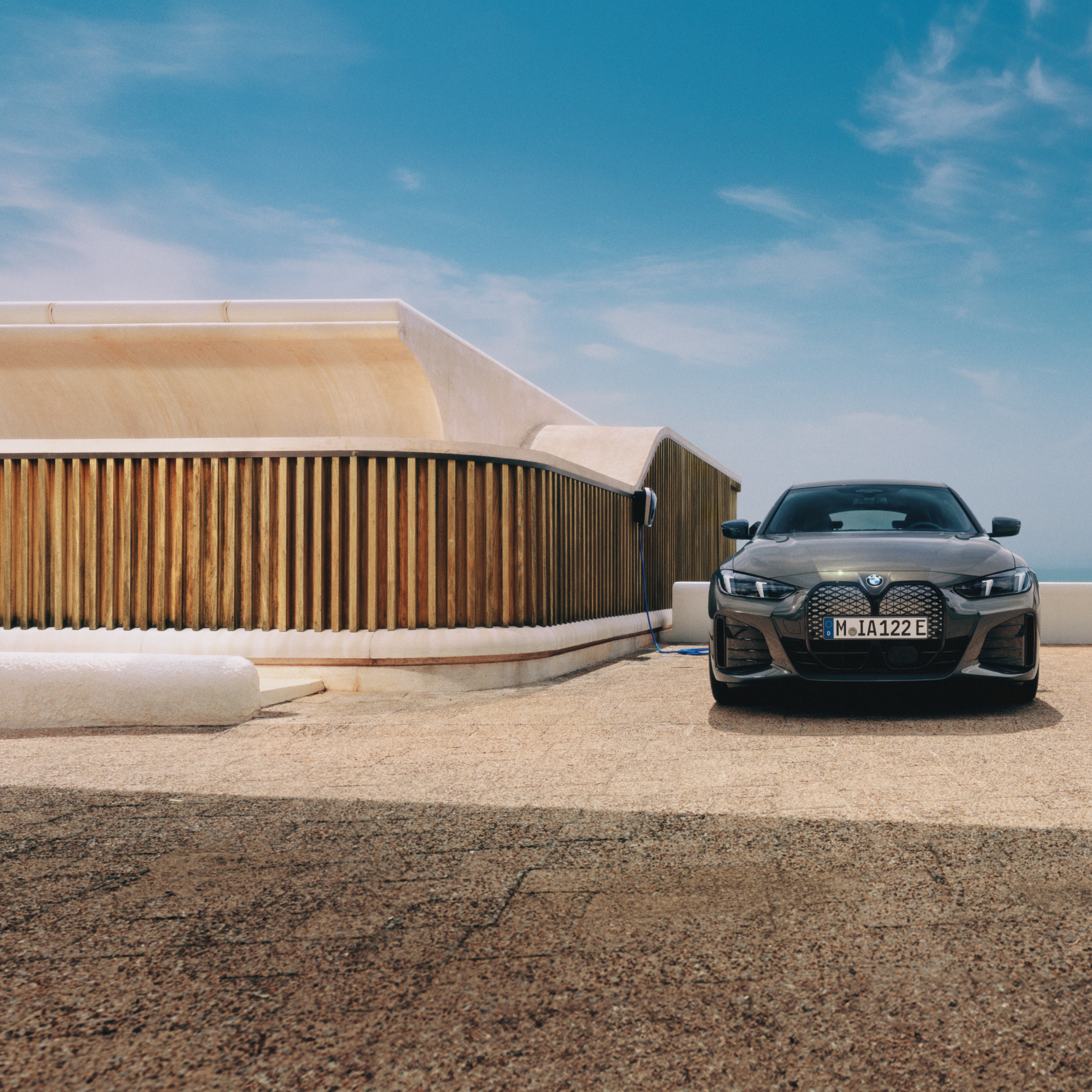 ผู้ชายถือสมาร์ทโฟนยืนอยู่ข้างรถยนต์ BMW i4 ซึ่งกำลังชาร์จกับ Wallbox
