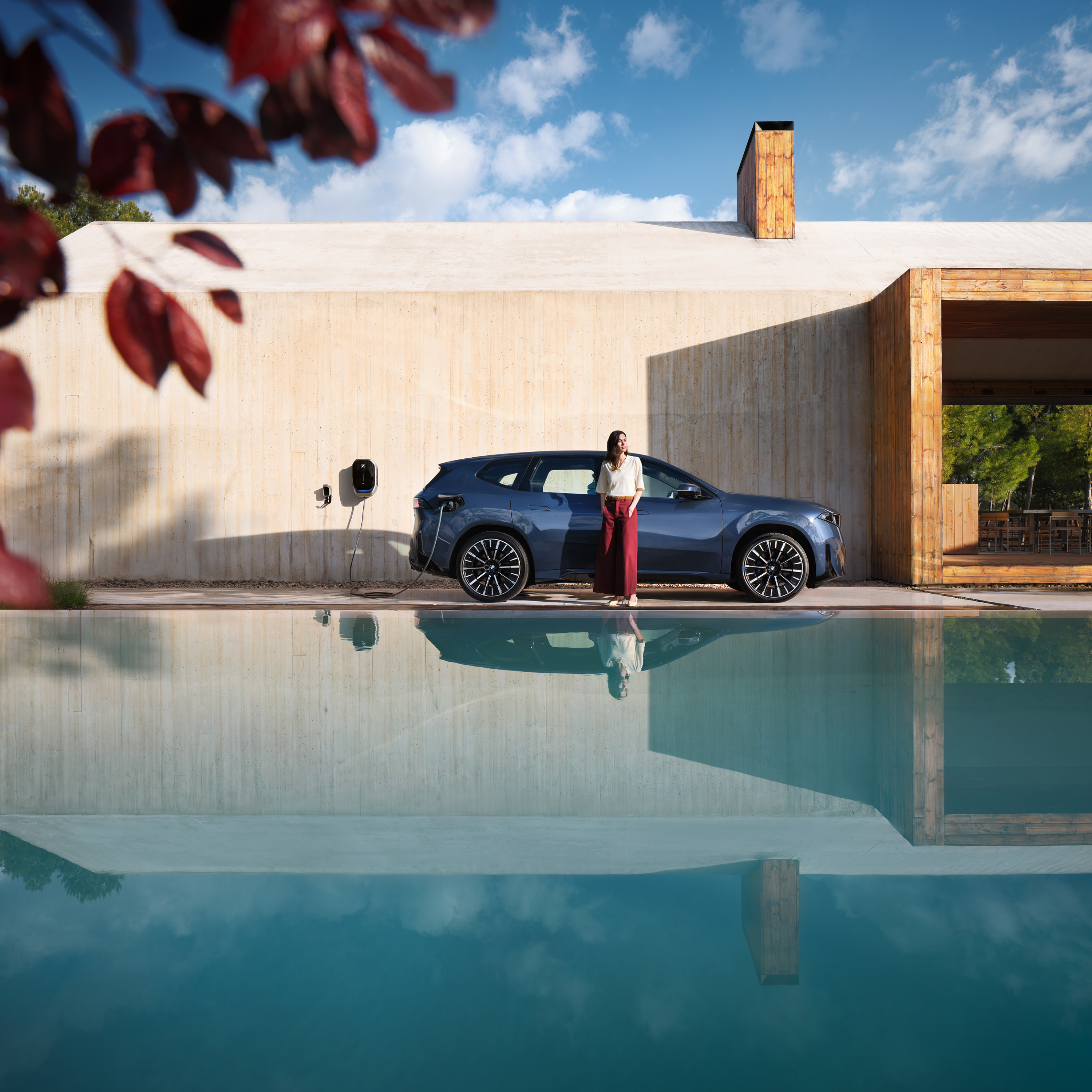 ผู้หญิงกำลังยืนอยู่หน้ารถยนต์ BMW iX3 ที่กำลังชาร์จกับ Wallbox