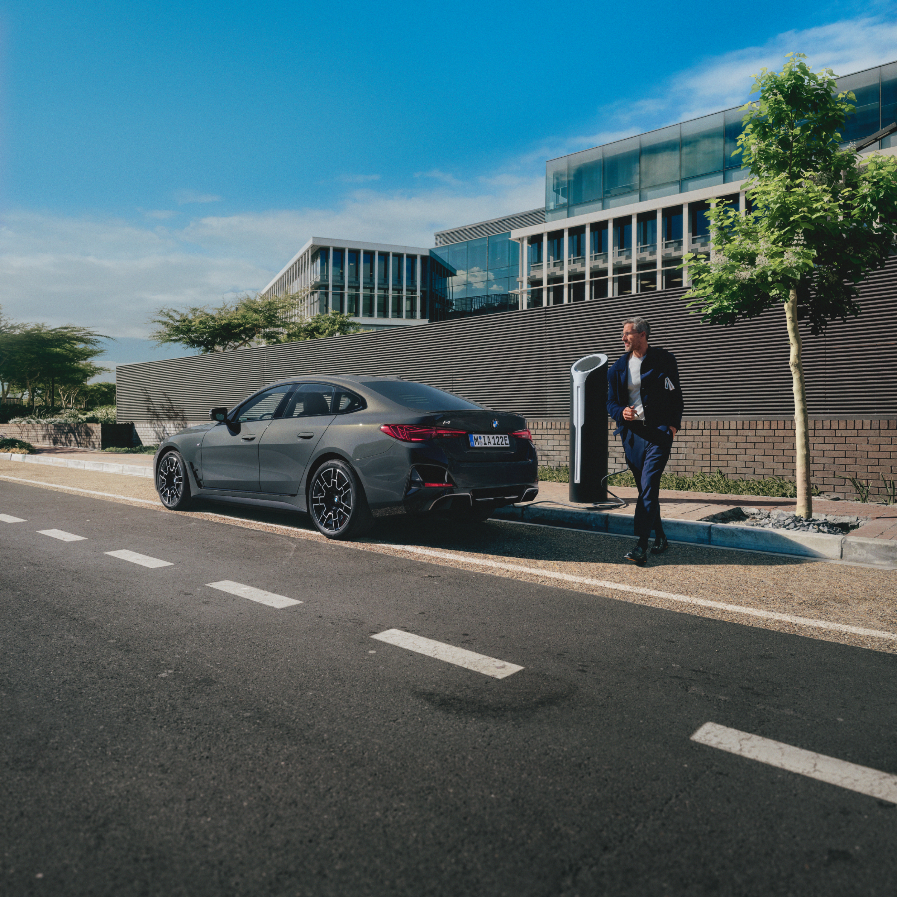 คนยืนอยู่หลังรถยนต์ BMW ที่กำลังชาร์จอยู่ริมถนน